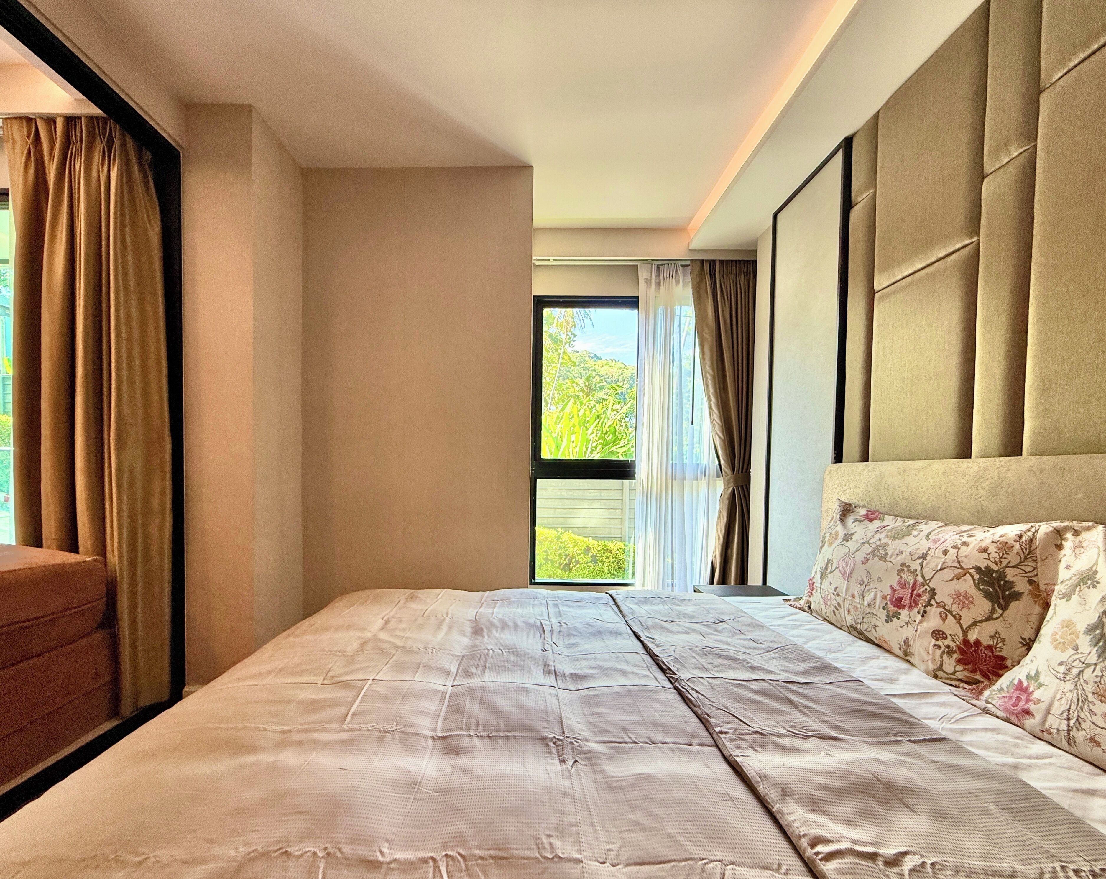 A bedroom with a large bed, a headboard, and a view of greenery outside.