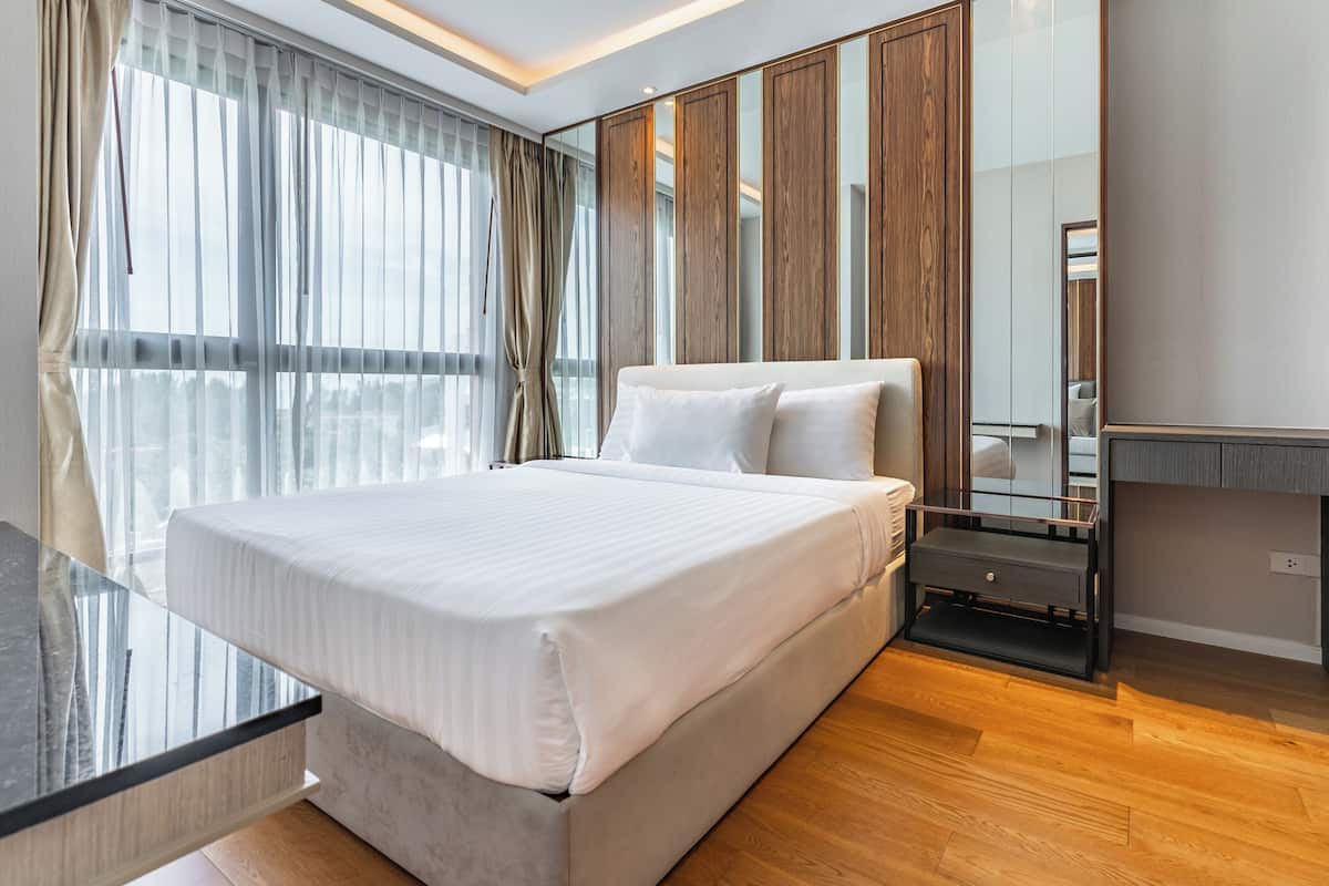 Ein modernes Hotelzimmer mit einem großen Bett, einem Glastisch und Blick auf die Stadt durch große Fenster.