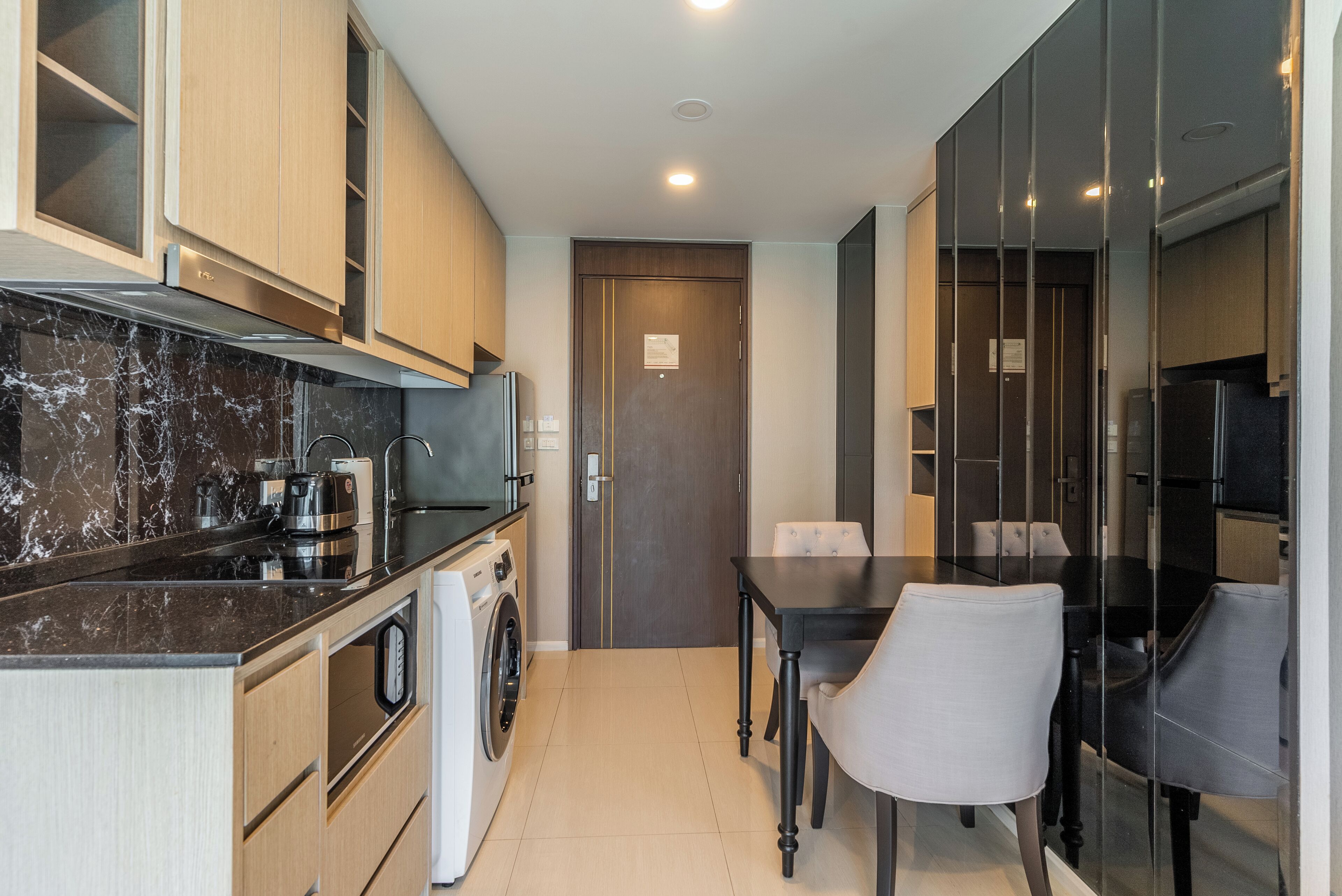 A compact kitchen with a washing machine, a coffee maker, and a dining area with a table and chairs.