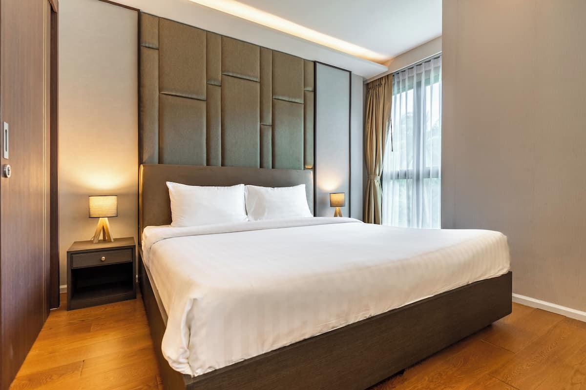 Ein modernes Hotelzimmer mit einem großen Bett, Holzboden, einem Kopfteil mit geometrischen Mustern und zwei Nachttischlampen.