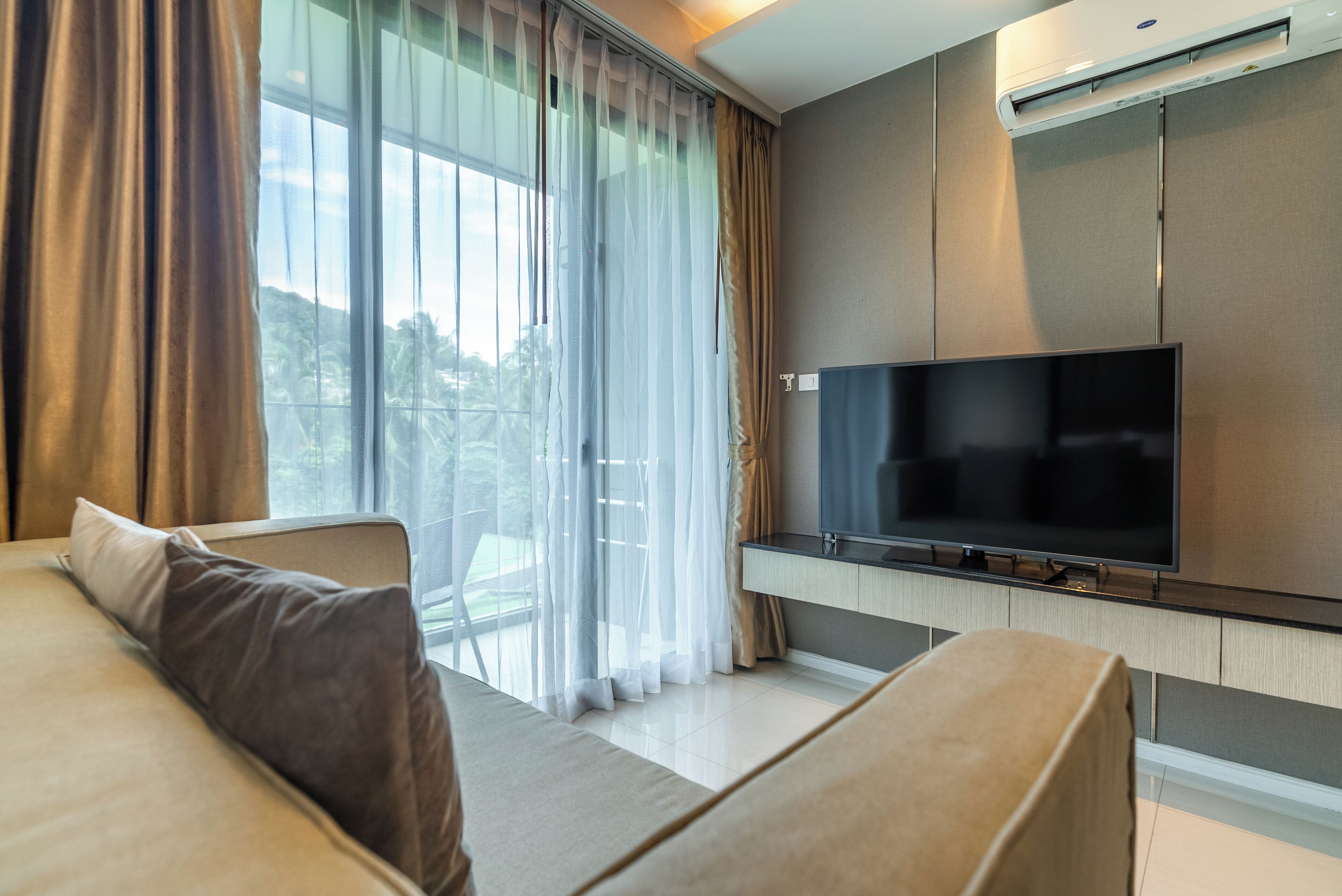 Una habitación de hotel moderna con un televisor de pantalla plana grande, un sofá y un ventanal con cortinas translúcidas.