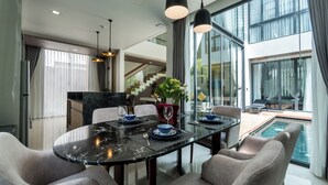 Ein moderner Essbereich mit einem schwarzen Marmortisch, grau gepolsterten Stühlen und Pendelleuchten. Eine Glasstaircase führt zu einem Balkon mit Blick auf einen Pool.