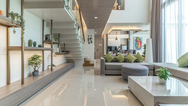A modern interior with a staircase, a living area with a sofa and cushions, and a kitchen in the background. - Panora Villa 8119 By Villacarte (Choeng Thale)