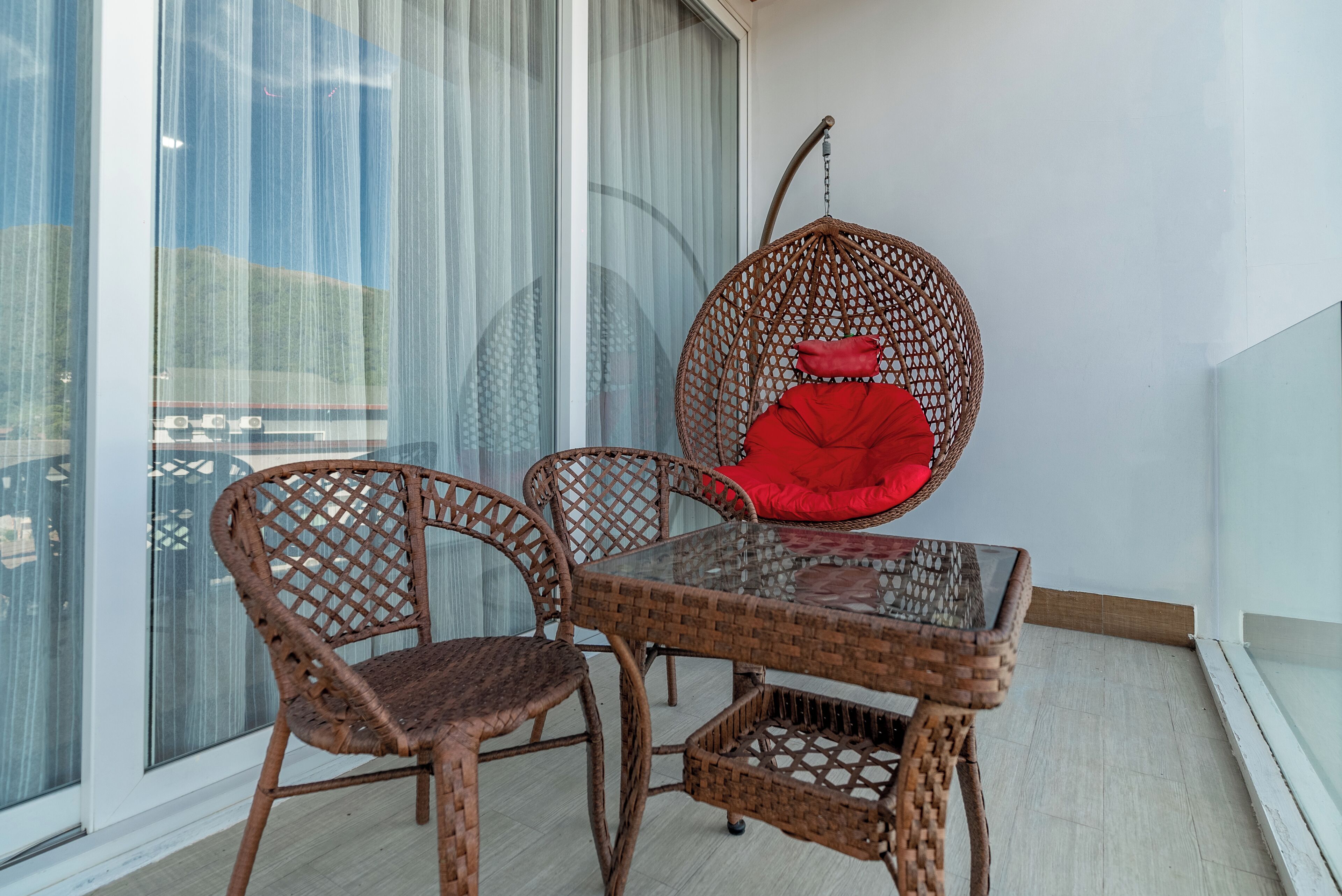 A balcony with wicker furniture, including a table and chairs, and a hanging chair with a red cushion.