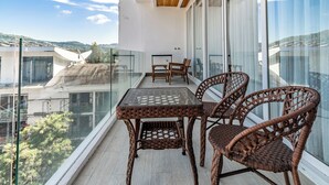 Un balcón con mobiliario de mimbre, una mesa de vidrio y vistas a la ciudad.