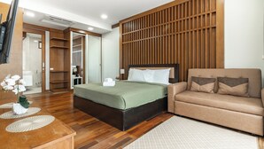 Una habitación de hotel moderna con suelo de madera, una cama con ropa de cama verde, un sofá beige y un mamparo de madera.