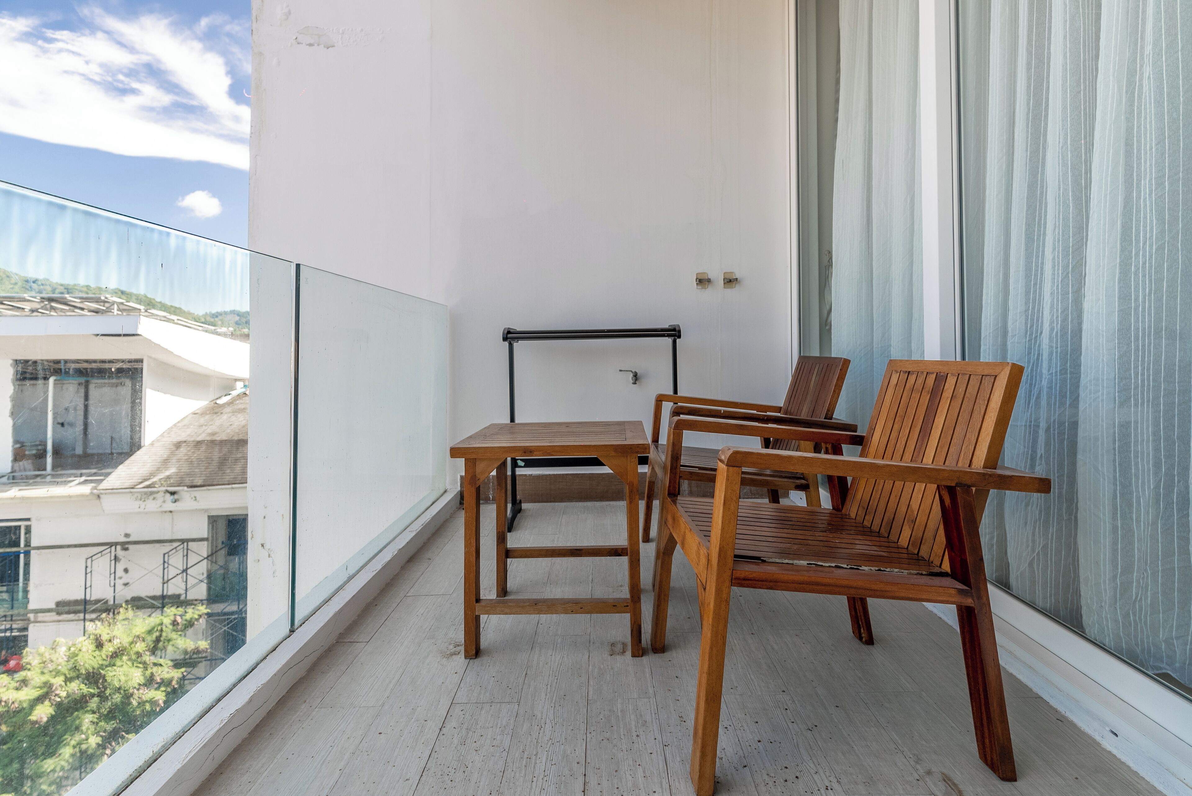 A balcony with a wooden table and chairs, a metal towel rack, and a view of buildings and trees.