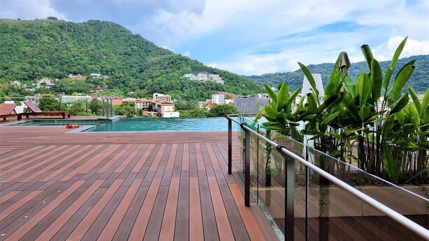 Una terraza de madera con piscina, rodeada de abundante vegetación y un paisaje montañoso.