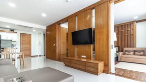 Una sala de estar moderna con un sofá, paneles de madera, un televisor y un comedor con una mesa y sillas.