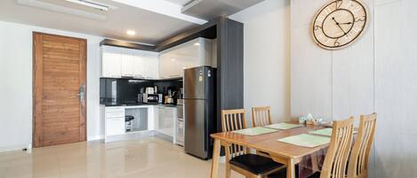 A modern kitchen with a refrigerator, stove, and microwave. There is a dining table with chairs and a clock on the wall.