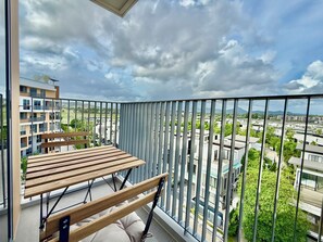 A balcony with a wooden table and bench, overlooking a residential area with buildings and greenery. - Skypark by Villacarte (Laguna)
