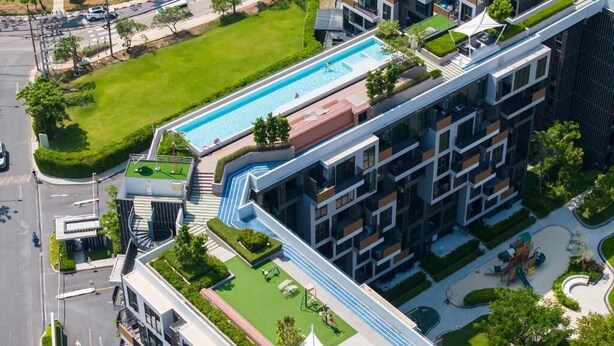 Ein modernes Mehrgeschosshaus mit Pool auf dem Dach, begrünten Terrassen und einem Fußweg.