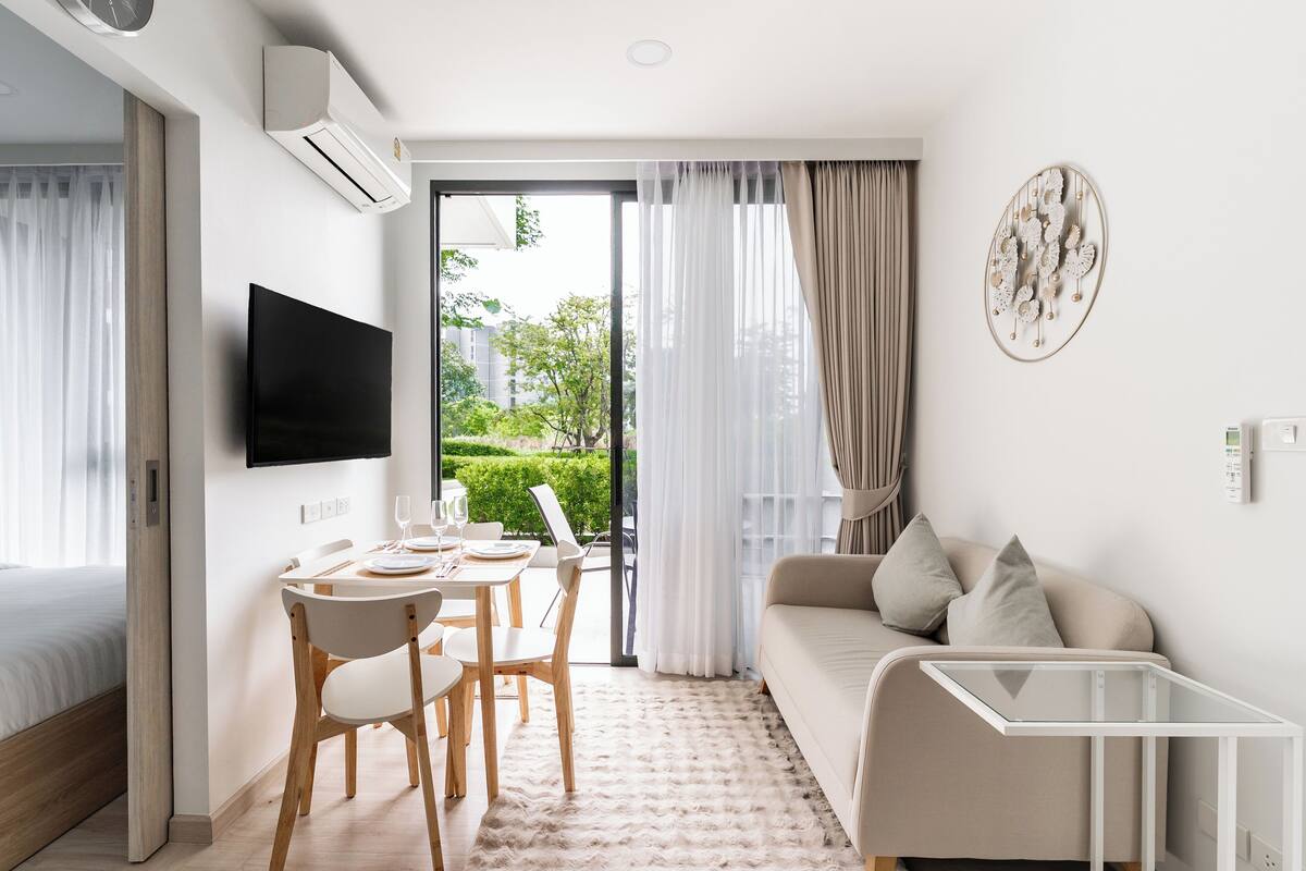 Une chambre d’hôtel moderne dotée d’une télévision à écran plat, d’un coin repas avec une table et des chaises, d’un canapé et d’une table basse en verre.