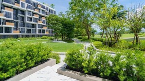 Ein modernes Gebäude mit mehreren Balkonen und einem gepflegten Garten mit Bäumen und Sträuchern.