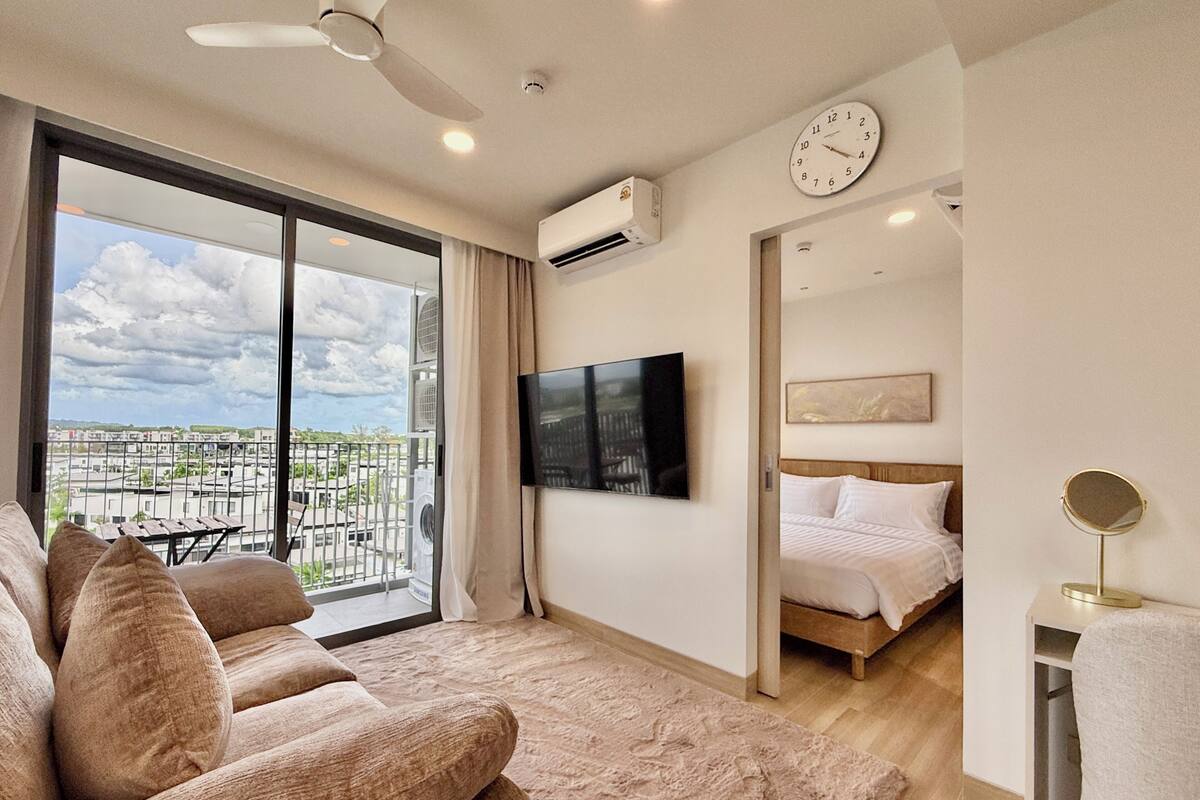 Une chambre d’hôtel moderne dotée d’un balcon, d’un téléviseur à écran plat, d’un lit et d’un miroir rond.