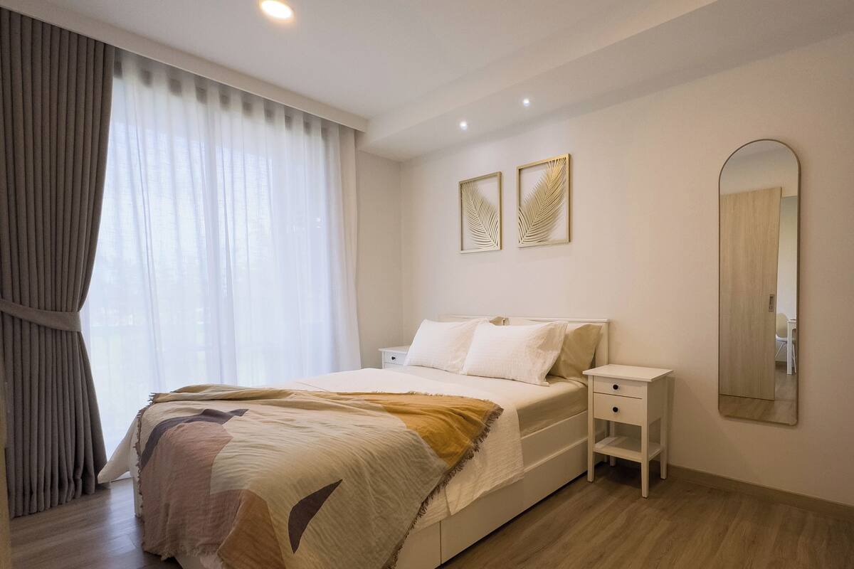 Une chambre moderne avec un grand lit, une table de chevet, une commode, un miroir et deux œuvres d’art accrochées au mur.