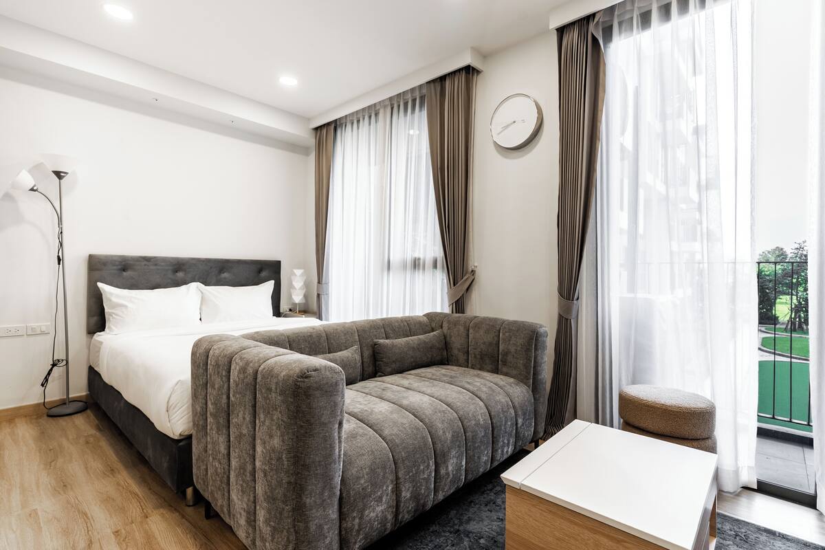 Une chambre d’hôtel moderne équipée d’un lit, d’un canapé, d’une table de chevet et offrant une vue sur un espace extérieur verdoyant.