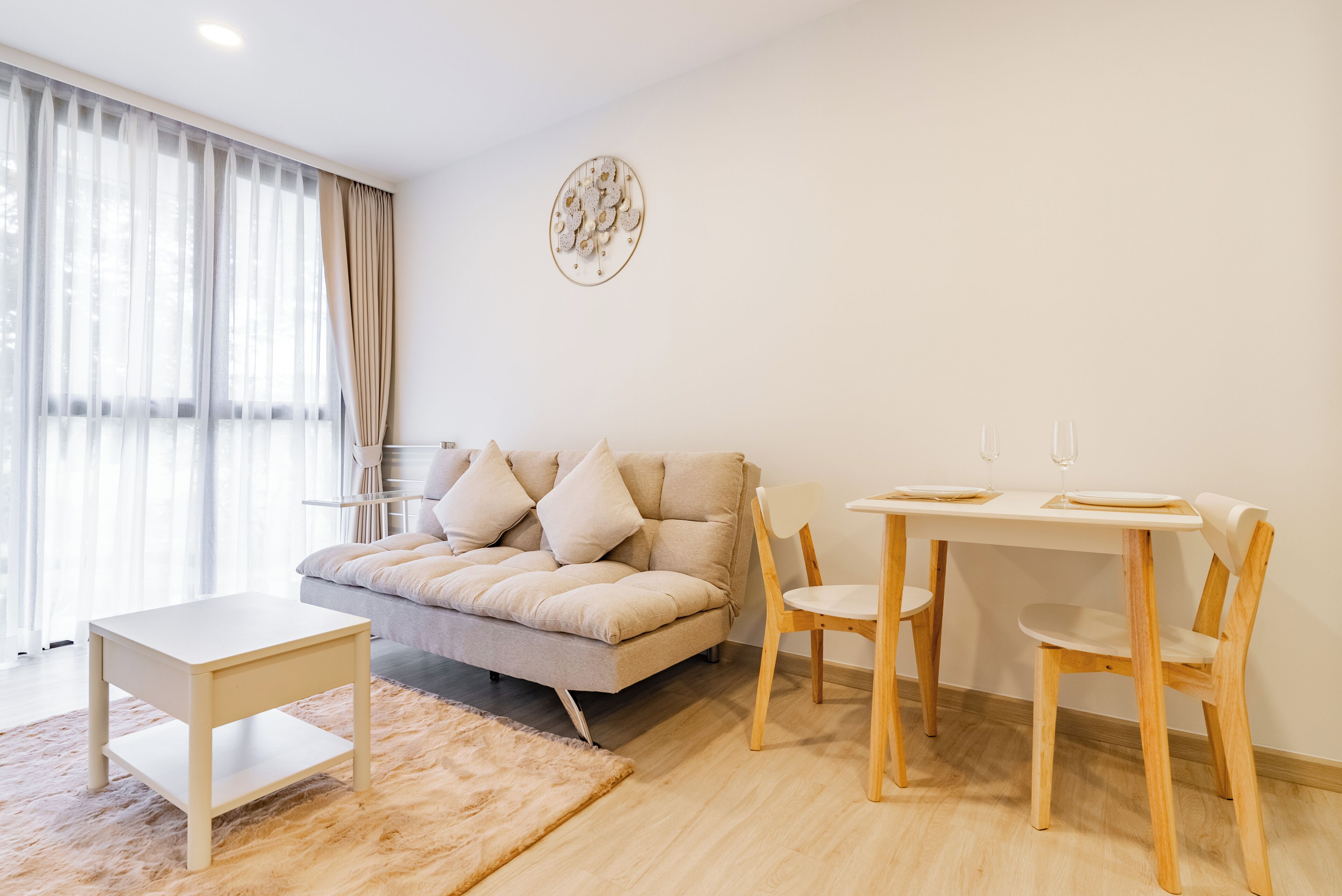 A living room with a sofa, a small table, two chairs, a rug, and a wall-mounted decoration.