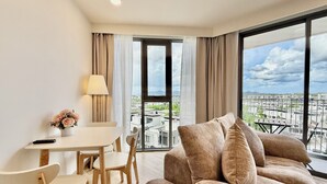 Ein modernes Wohnzimmer mit einer Couch, einem Esstisch mit Stühlen, einer Lampe und Blick auf eine Skyline durch große Fenster.