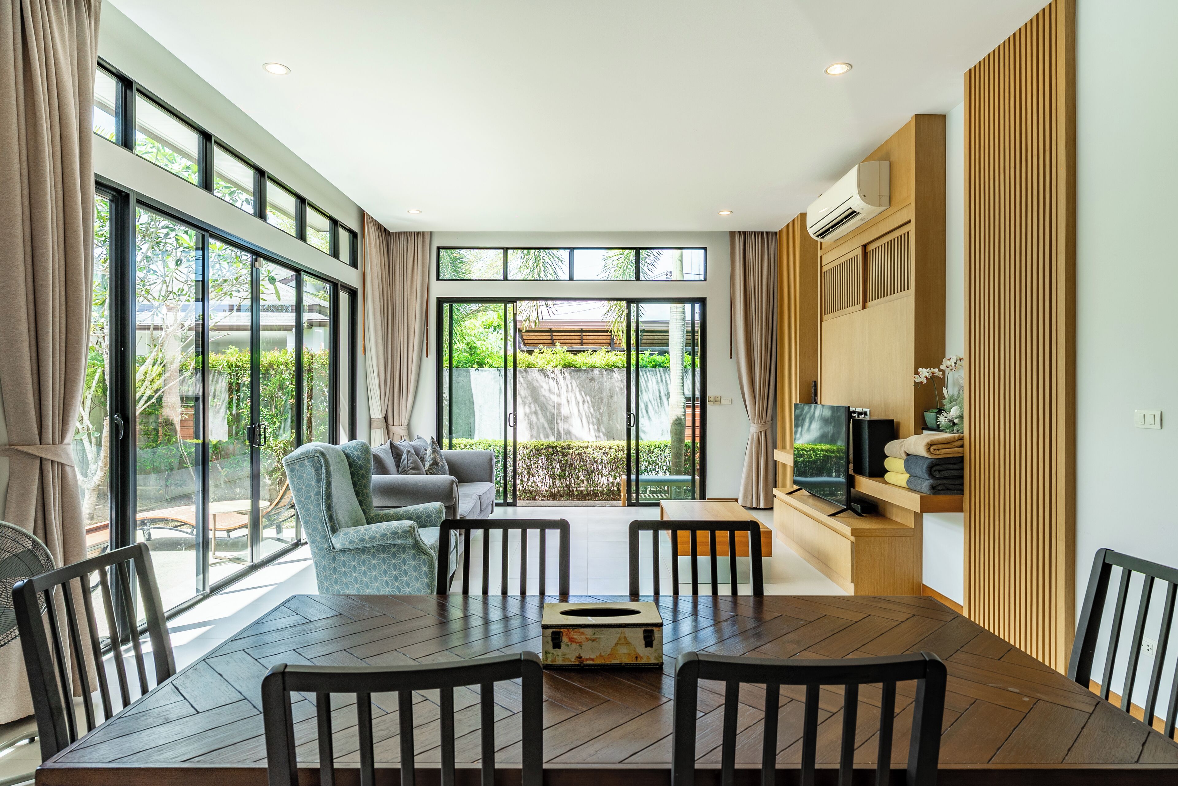 A modern living room with a dining area, large windows, and a television.