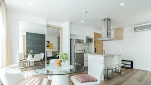 Une cuisine moderne équipée d’un réfrigérateur, d’un four à micro-ondes et d’une cuisinière en acier inoxydable. On y trouve une table à manger en verre, des chaises blanches et une plante en pot.