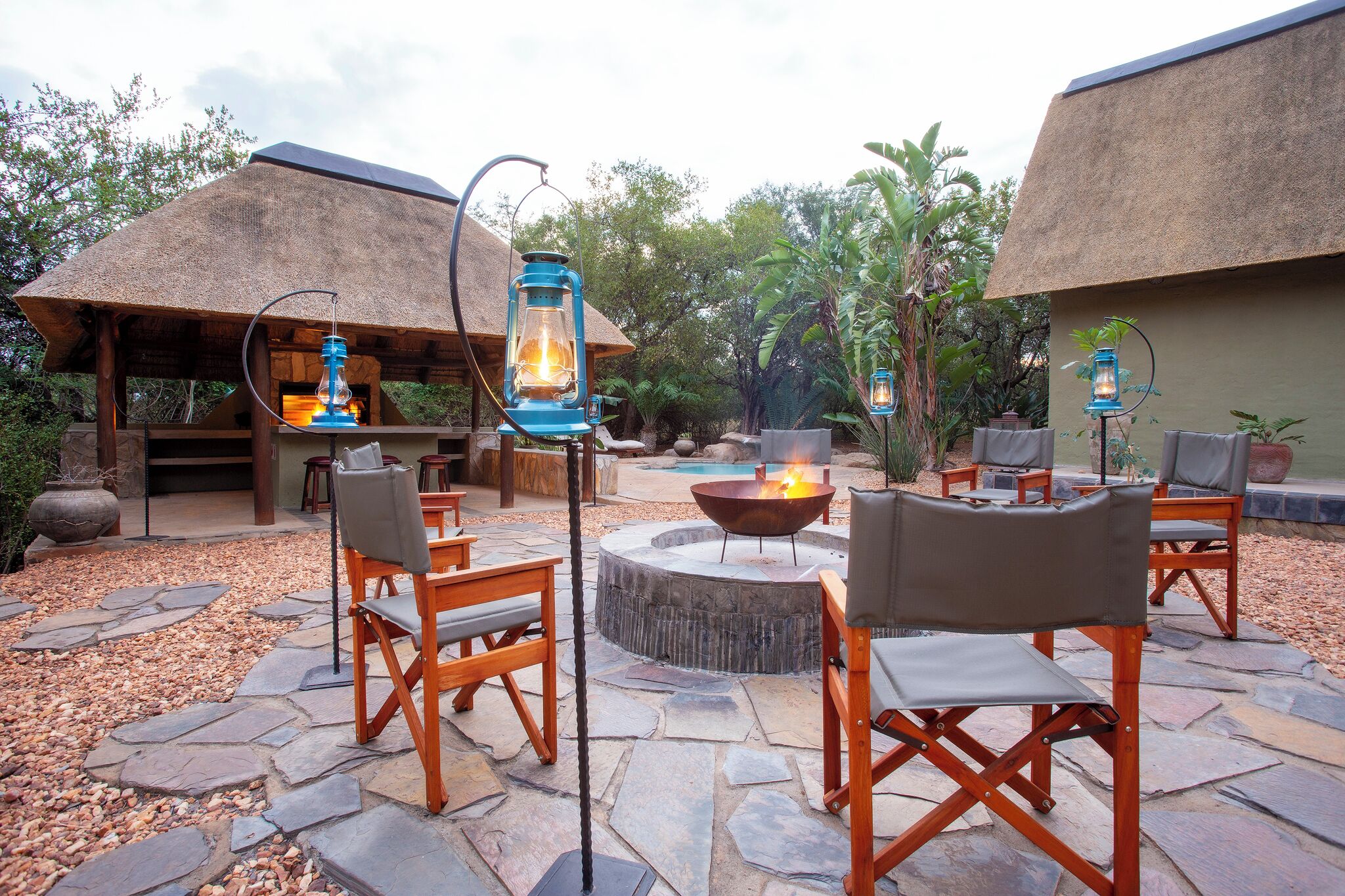 An outdoor patio area with stone flooring, wooden chairs, a fire pit, and lanterns.