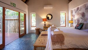 A room with a bed, a wooden table, a lamp, a wall clock, and a window. - ETNIKA MANOR HOUSE (Hoedspruit)