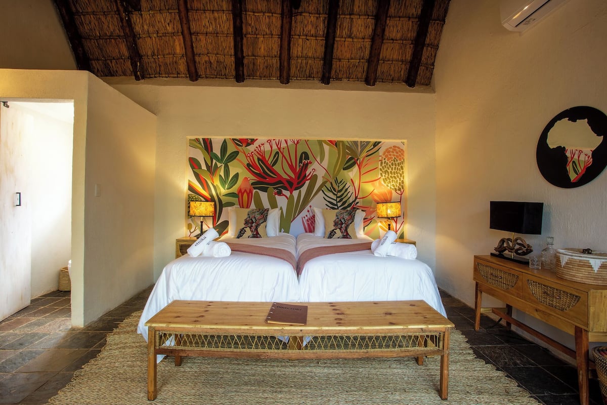 A room with a bed, a wooden bench, a bedside table with a lamp, and a wall-mounted TV.
