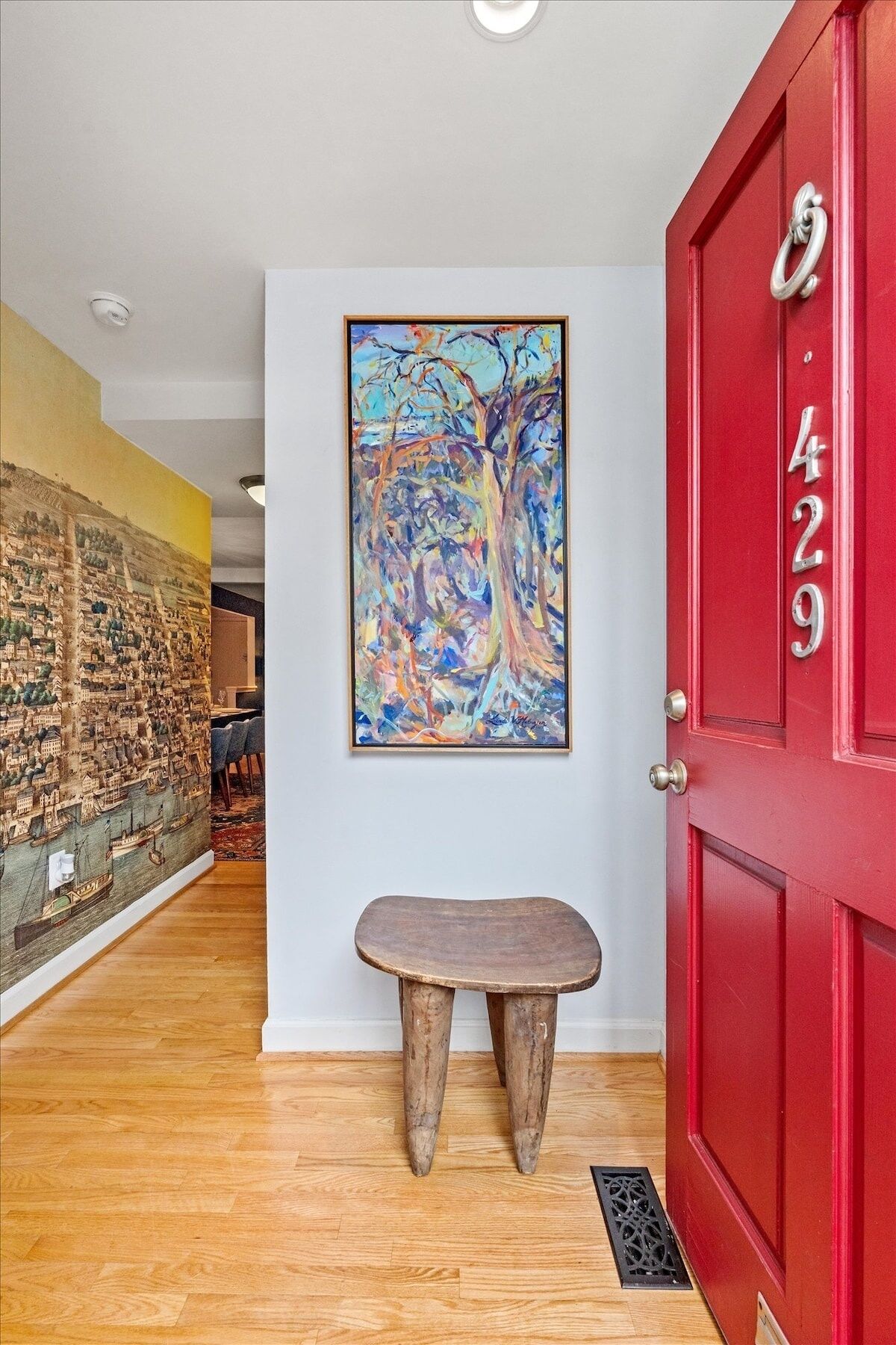 A hallway with a red door marked "429", a wooden bench, and a colorful abstract painting on the wall.