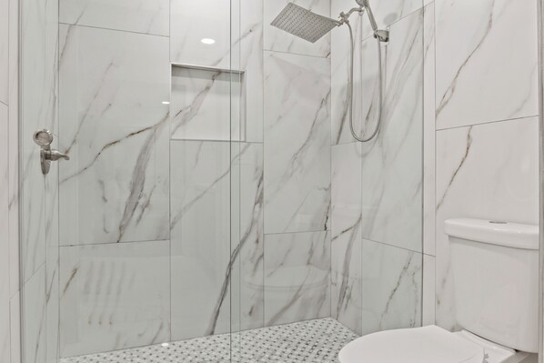 Une salle de bain moderne avec douche, toilettes et carrelage au sol.