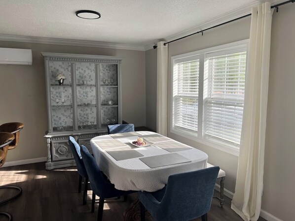 A dining area with a table set for four, a decorative cabinet, and a window with blinds.