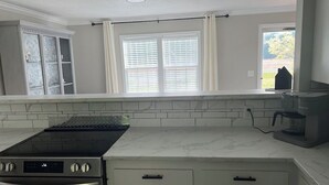 A kitchen with a built-in stove, white cabinets, and a window with blinds. - Relaxing 3-Bedroom Getaway in Peaceful Cades – Sleeps 8 (Cades)