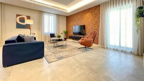 Ein modernes Wohnzimmer mit einer Couch, einem Sessel, einem Couchtisch und einem an einer Ziegelwand befestigten Fernseher.