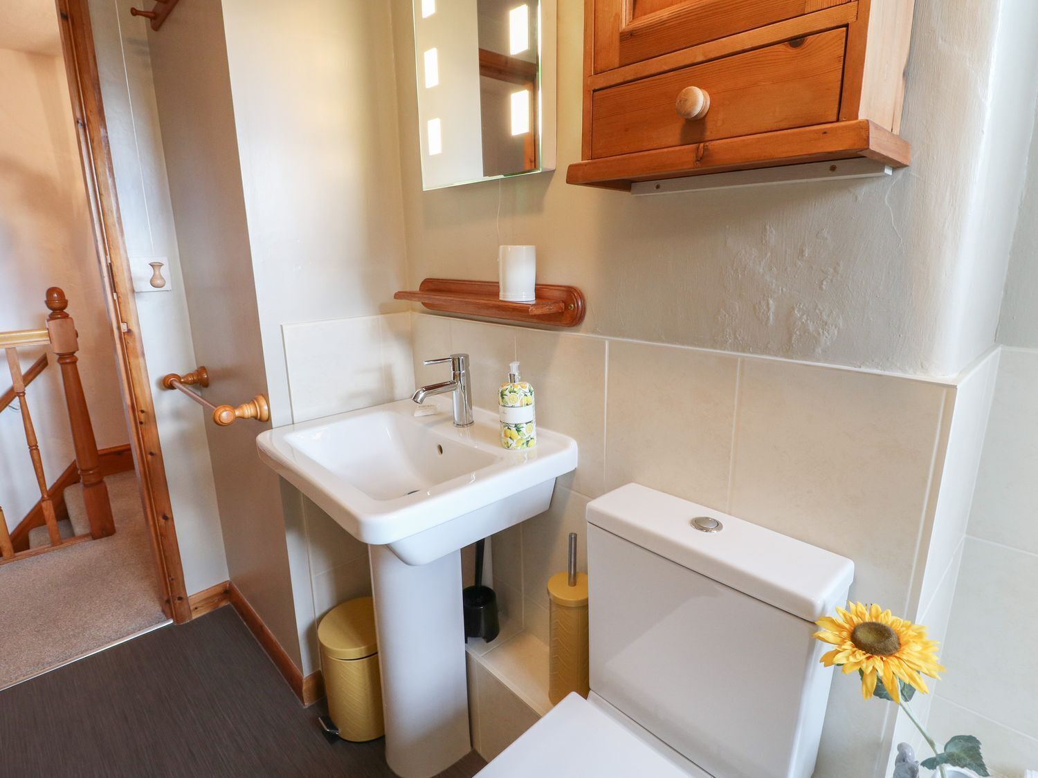 A bathroom with a white sink, a toilet, and a wooden cabinet above the mirror.