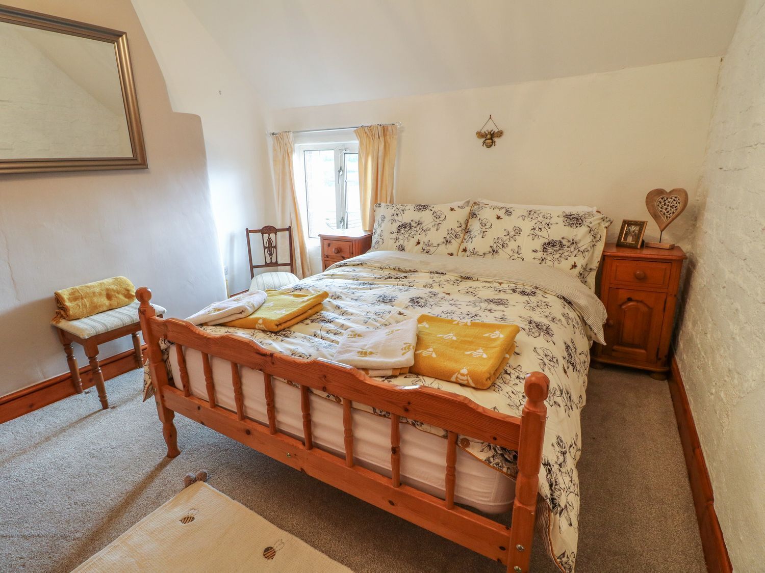 Une chambre à coucher avec un lit en bois, une table de chevet, une chaise et une fenêtre avec des rideaux.