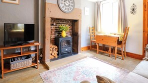 Ein Wohnzimmer mit Kamin, Fernseher auf einem Holzboden, einem Esstisch mit Stühlen und einem gemusterten Teppich.