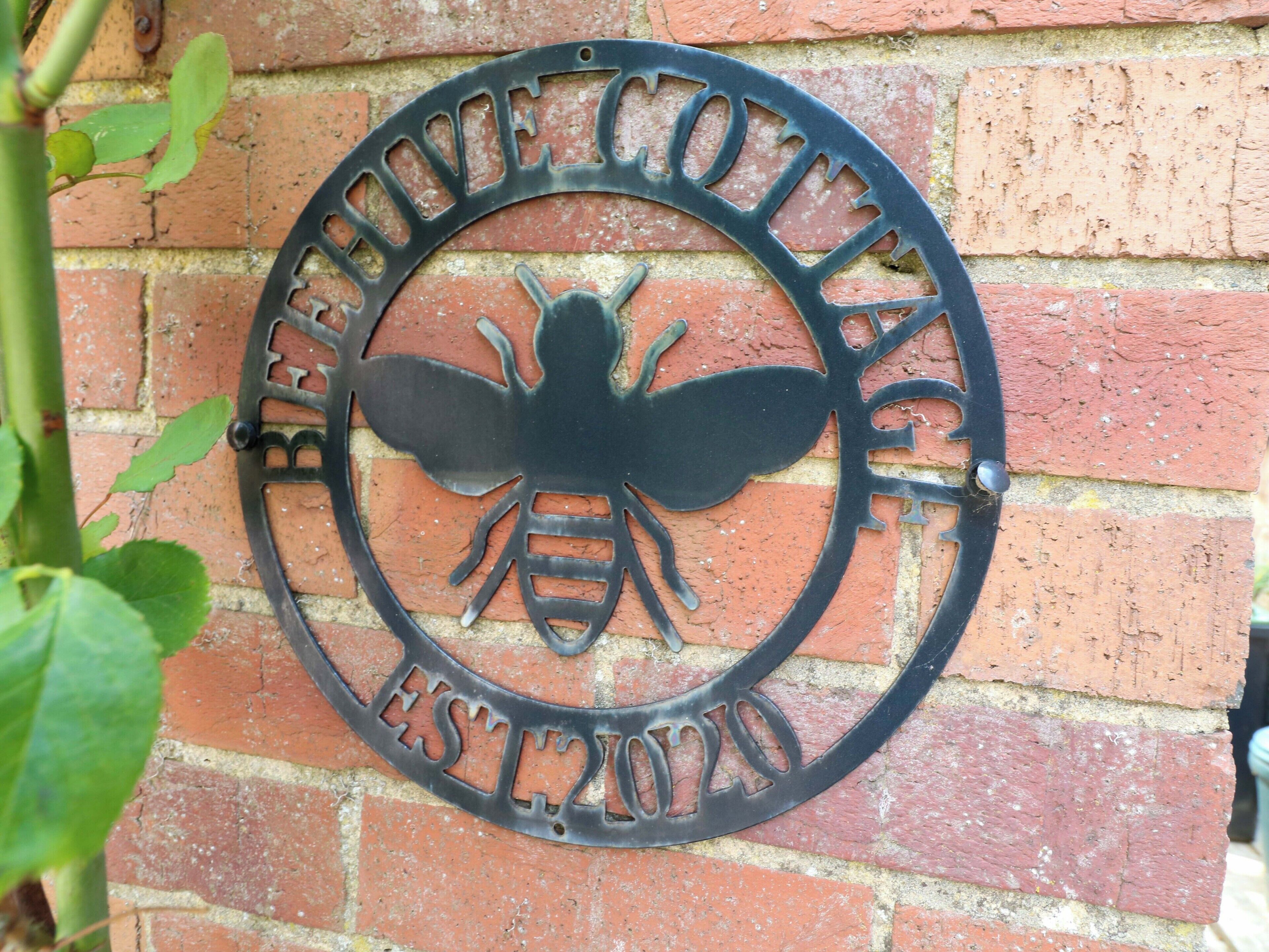 A circular metal plaque with a bee design and the text "Beehive Cottage" and "Established 2010".