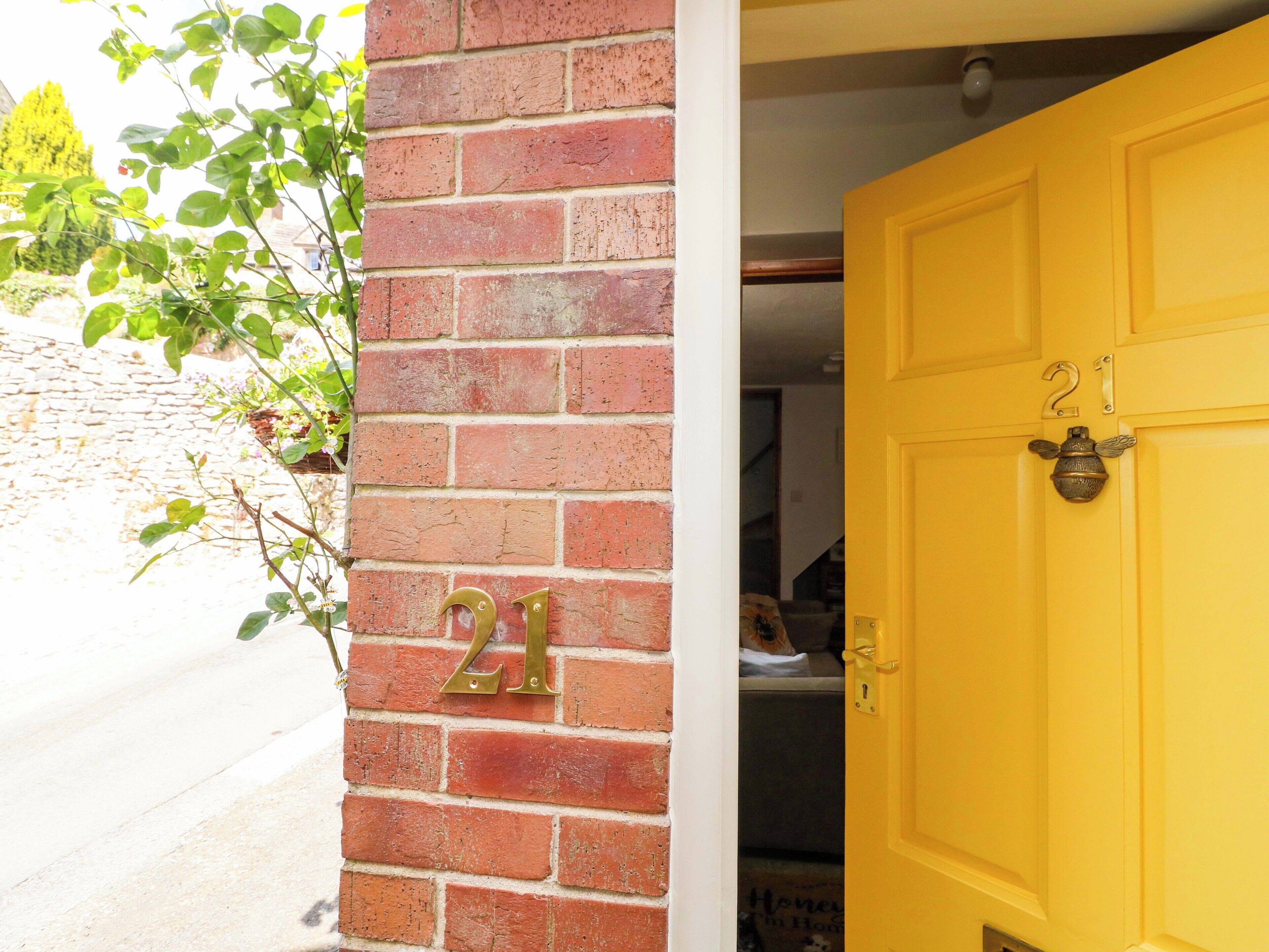 Une porte jaune portant le numéro 21, un mur de briques et une plante aux feuilles vertes.