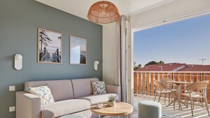Un salon moderne avec un canapé, une table basse ronde et un balcon aménagé avec des sièges d’extérieur.