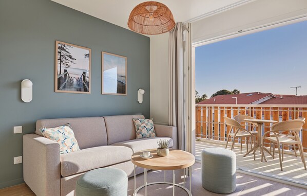 A modern living room with a sofa, a round coffee table, and a balcony with outdoor seating.