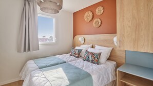 A bedroom with a bed, a window with curtains, a wooden headboard, and wall decor.
