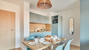 A modern kitchen with light blue cabinets, a wooden dining table set for four, and a wicker ceiling light.