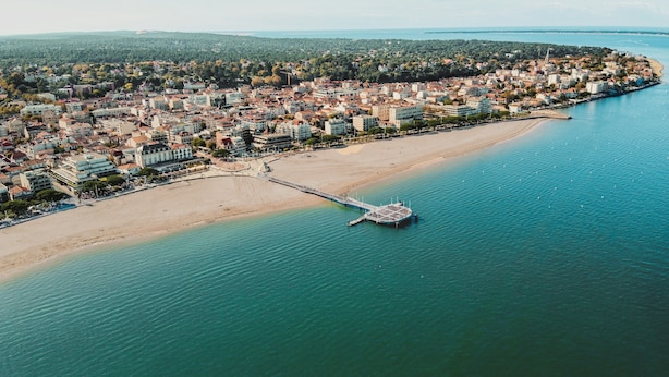 An aerial view of a coastal city with a beach, a pier, and dense urban buildings.