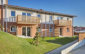 Un moderno edificio residencial de varios pisos con balcones, ventanas grandes y techo inclinado.