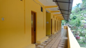 A corridor with yellow walls and a patterned floor, leading to a covered area with potted plants. - Hotel Him Deep Uttarkashi (Bhatwari)