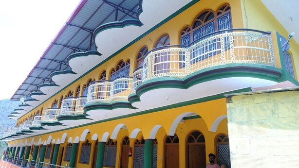 A building with multiple balconies and arched windows, featuring a yellow facade and green accents. - Hotel Him Deep Uttarkashi (Bhatwari)