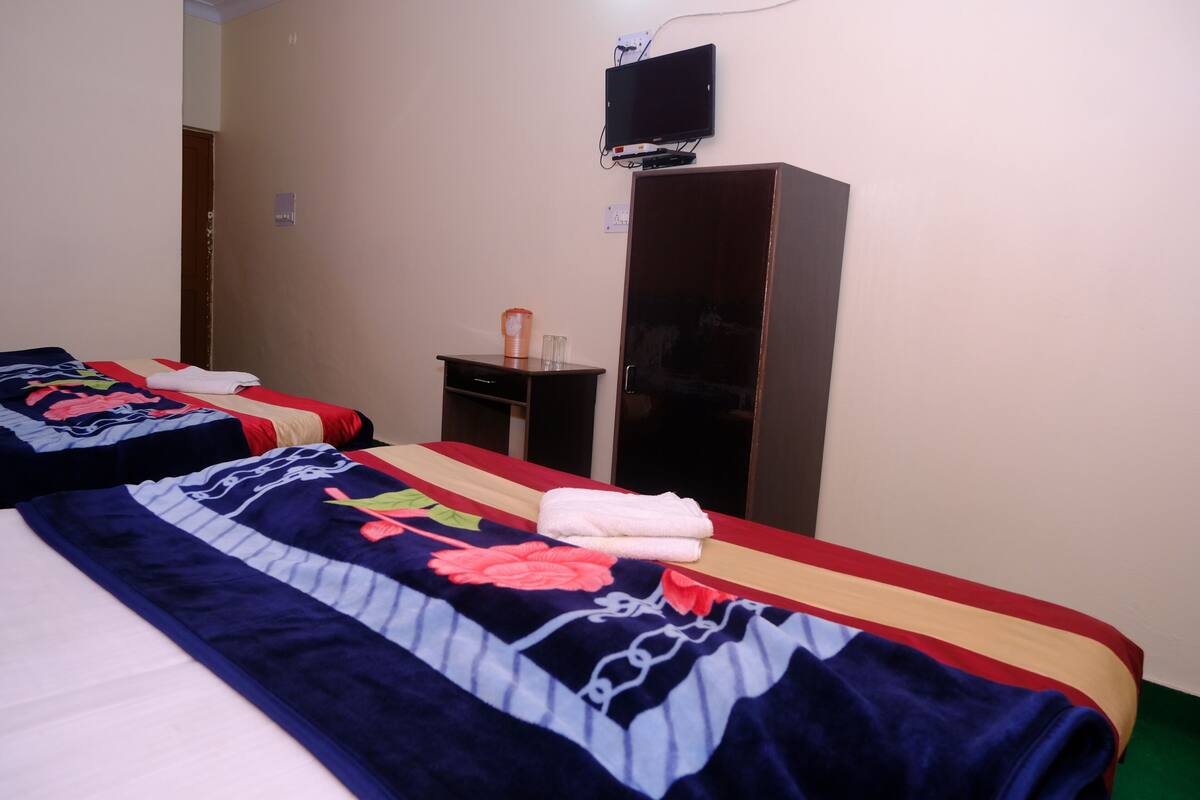 A hotel room with two beds, a TV mounted on the wall, and a wardrobe.