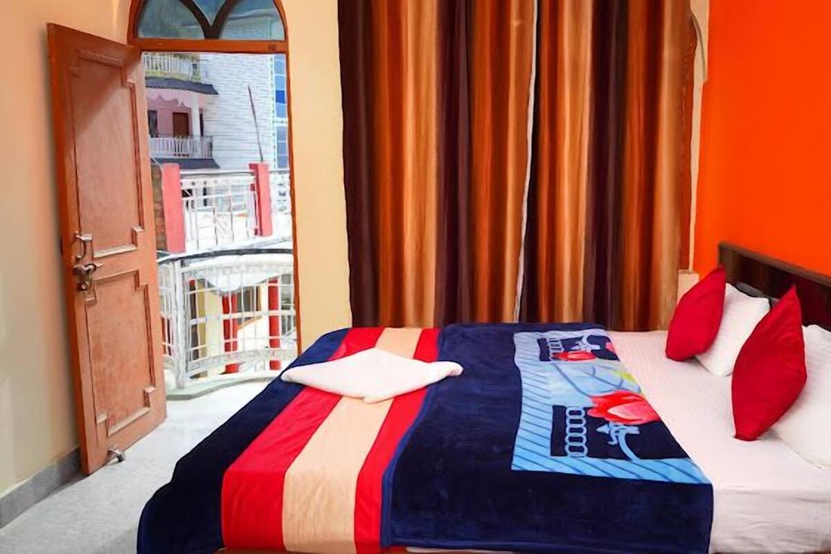 A hotel room with a bed, orange walls, and a view of a balcony with buildings.