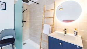 Un baño moderno con ducha, lavamanos, espejo y una silla.