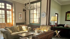 A room with a sofa, armchair, and a table. There is a clock on the wall and a chandelier. - Former French railway station with private swimming pool and WIFI (Blond)